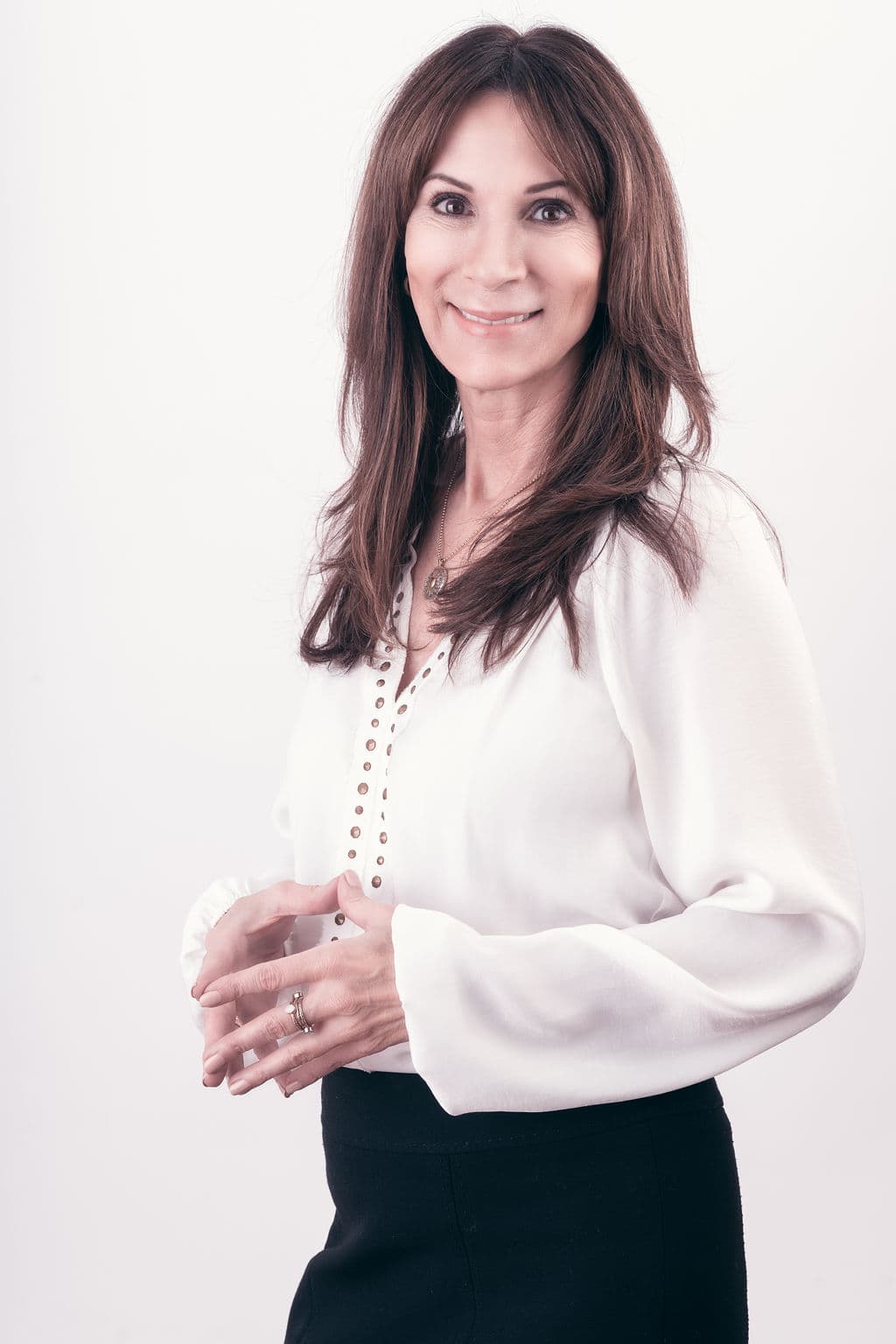 Smiling woman with long brown hair wearing white blouse and black skirt against white background.